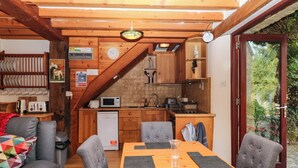 Een gezellige keuken met houten kastjes, een magnetron en een spoelbak. Er staat een eettafel met stoelen en een kleurrijke quilt op de bank.