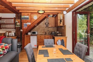 A cozy kitchen with wooden cabinets, a microwave, and a sink. There's a dining table with chairs and a colorful quilt on the couch. - Dashel Cottage at Dockwell Farm (Newton Abbot)