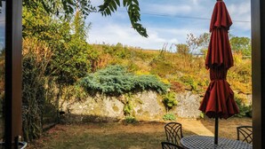 Een terras met een tafel, stoelen, een parasol en uitzicht op een tuin met een stenen muur.