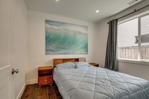A bedroom with a large bed, wooden nightstands, a wall-mounted painting of a wave, and a window with curtains. - Walk to Autzen Stadium: Eugene Getaway w/ Yard (Eugene)