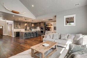 A spacious living area with a wooden coffee table, a grey sofa, and a kitchen with wooden cabinets and a large island. - Walk to Autzen Stadium: Eugene Getaway w/ Yard (Eugene)