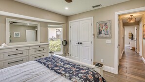 A bedroom with a bed, dresser, mirror, ceiling fan, and a hallway leading to another room. - Boat Dock & Outdoor Kitchen! Port Charlotte Escape (Port Charlotte)