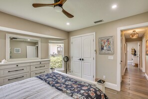 Ein Schlafzimmer mit Bett, Kommode, Spiegel, Deckenventilator und einem zur anderen Kammer führenden Gang.