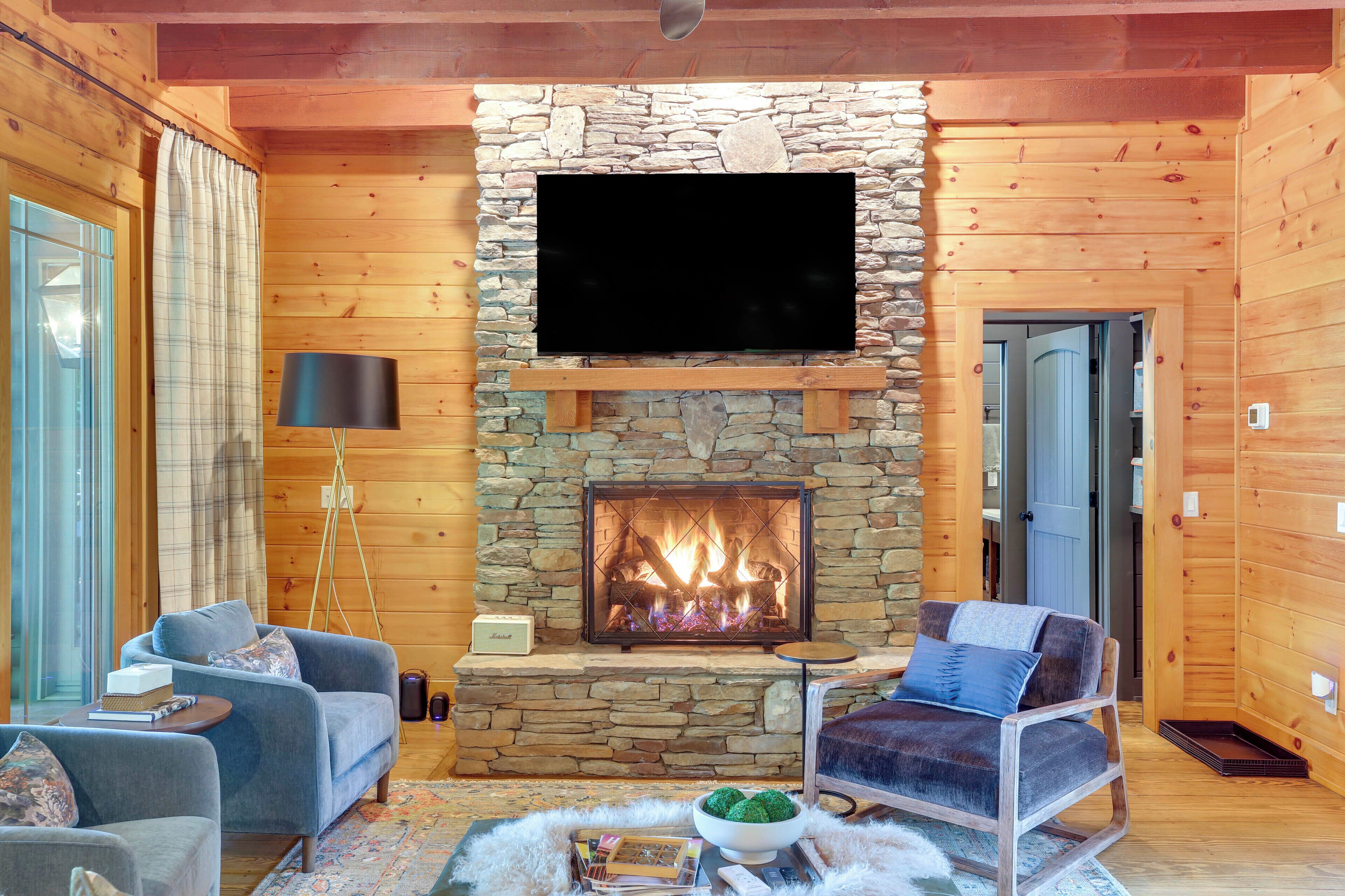 A cozy living room with a stone fireplace, a flat-screen TV, and two sofas.