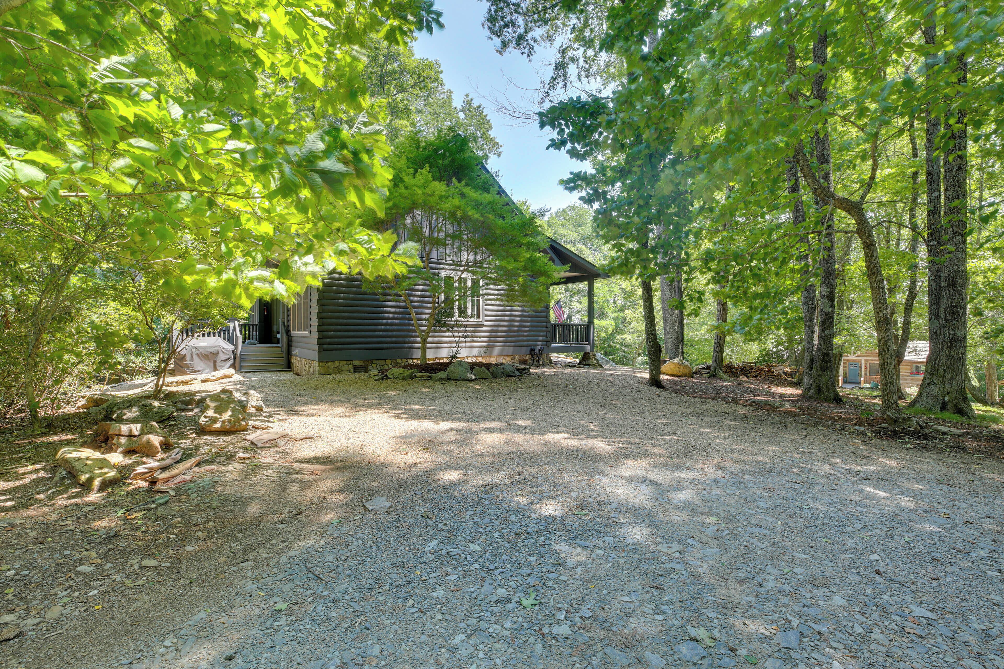 A rustic cabin with a gravel driveway, surrounded by dense trees.