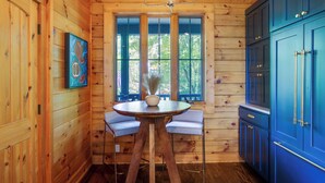 A wooden interior with a dining area, a large window, and blue cabinets. - Views, Hot Tub & Fire Pit! Luxe Blue Ridge Retreat (Blowing Rock)