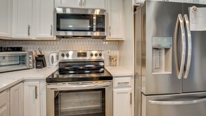 Eine moderne Küche mit weißen Schränken, einem Edelstahl-Kühlschrank, einem eingebauten Backofen, einer Mikrowelle und einem Toaster.