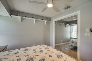 Quarto com cama, ventilador de teto, espelho e janela com persianas.