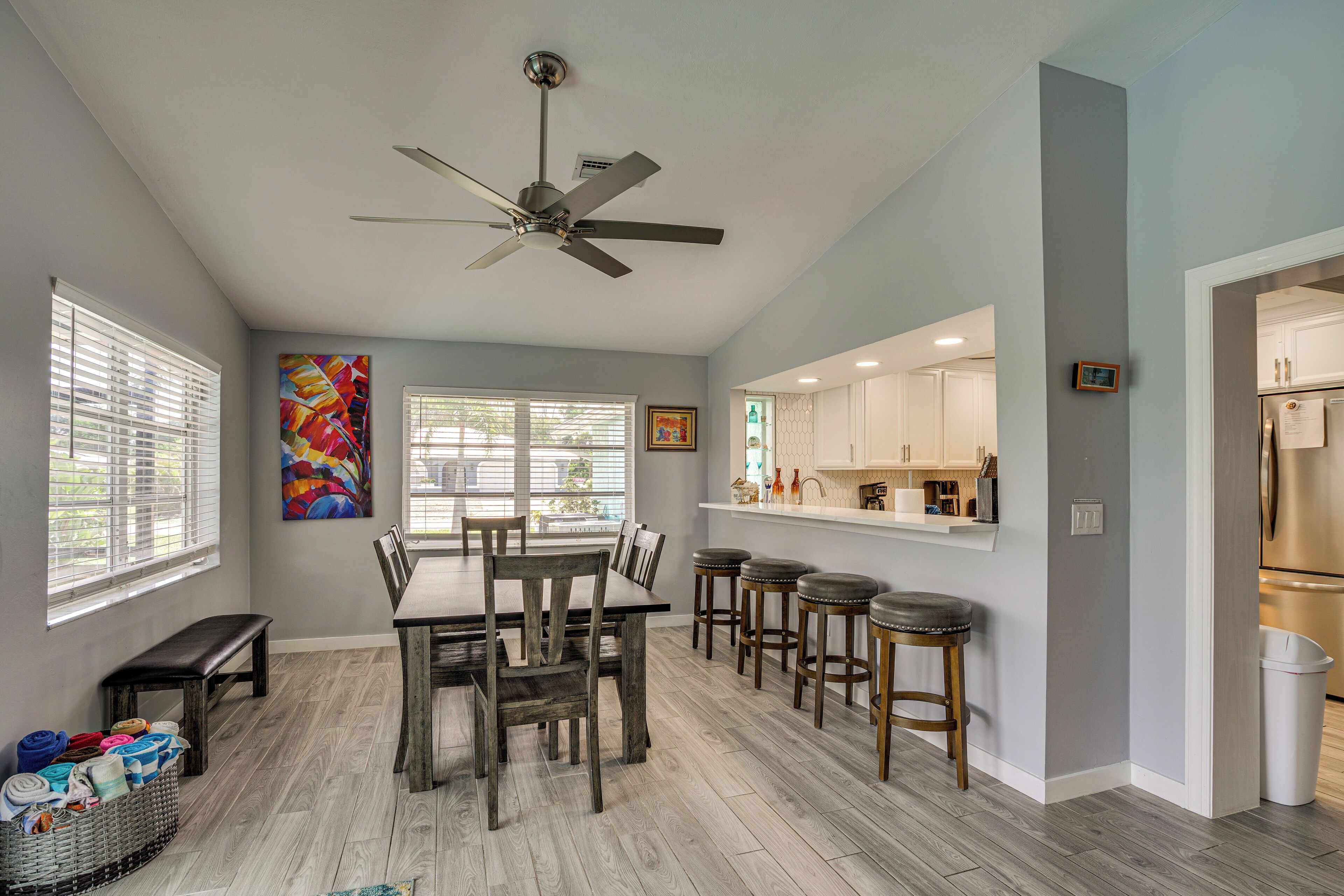 A modern kitchen with white cabinets, a stainless steel refrigerator, and a bar area with stools.