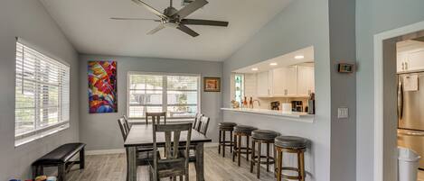A modern kitchen with white cabinets, a stainless steel refrigerator, and a bar area with stools.