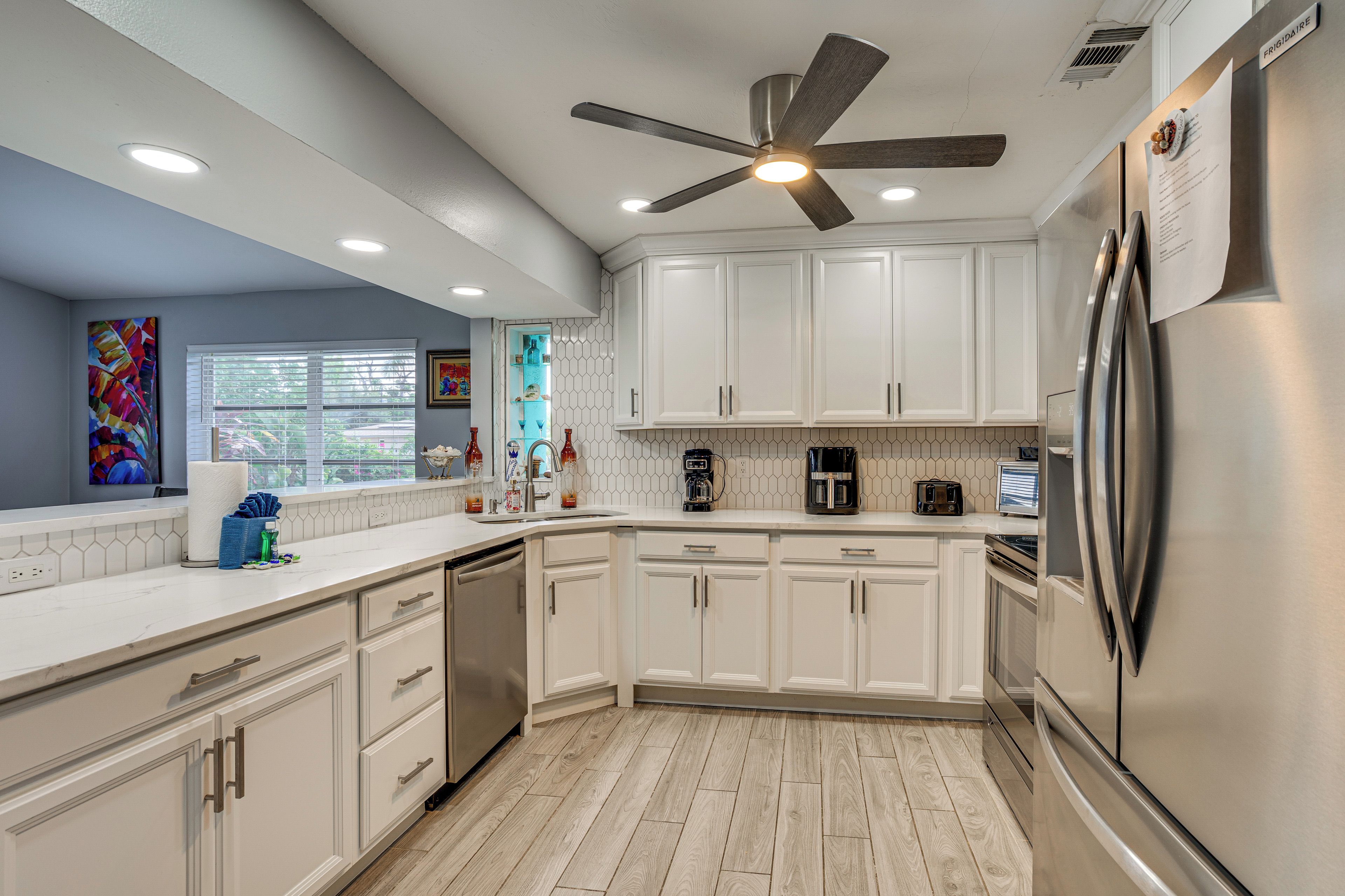 A modern kitchen with white cabinets, a stainless steel refrigerator, and a ceiling fan.