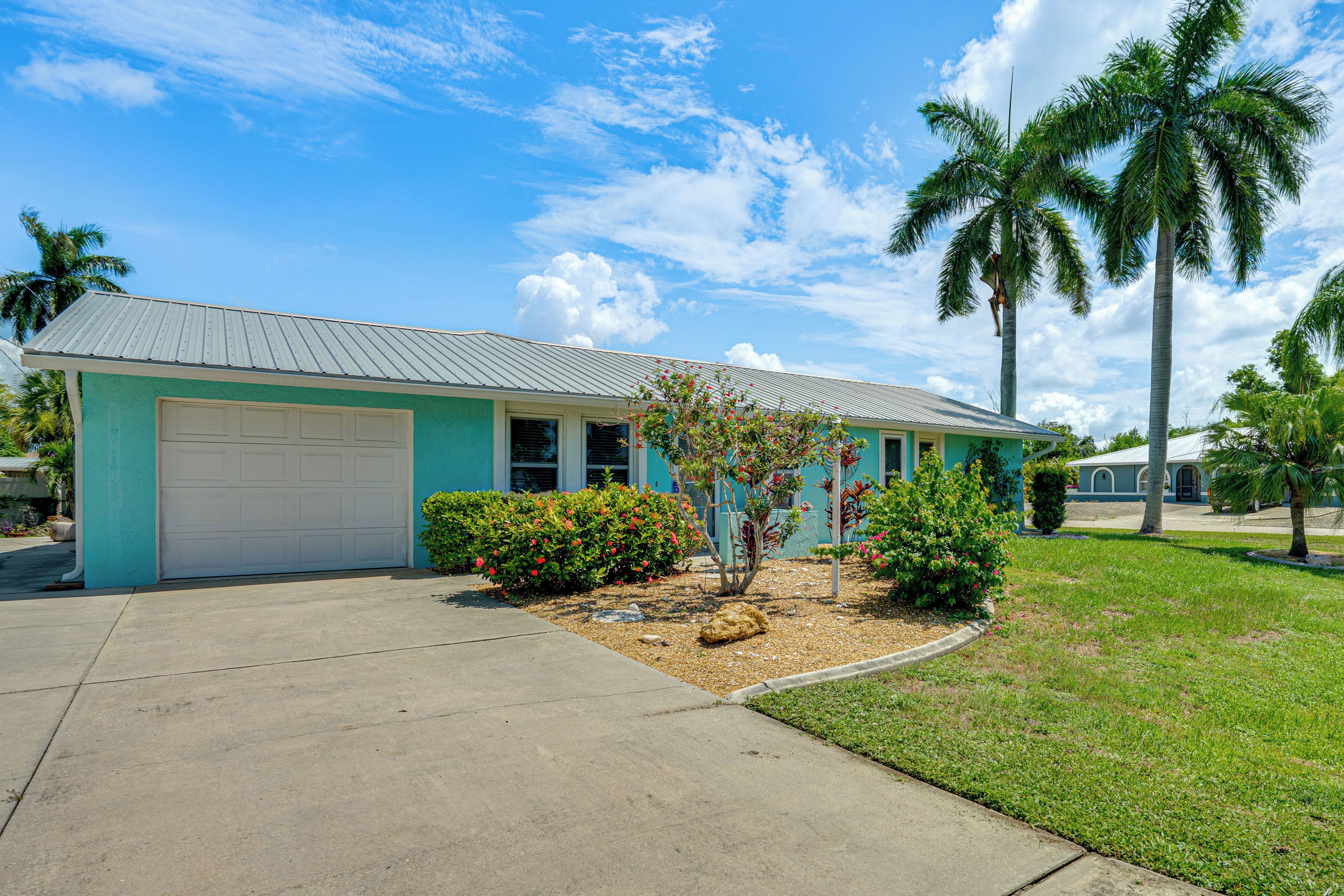 A single-story house with a garage, surrounded by a well-maintained lawn and palm trees.