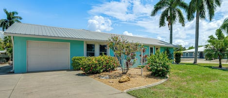 A single-story house with a garage, surrounded by a well-maintained lawn and palm trees.