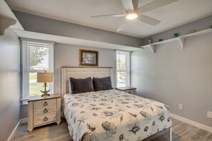 Ein Schlafzimmer mit Bett, Nachttischen, Deckenventilator und einem Fenster mit Jalousien.
