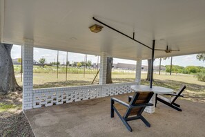 An outdoor patio area with a table and chairs, a brick wall, and a view of a grassy field and buildings in the distance.