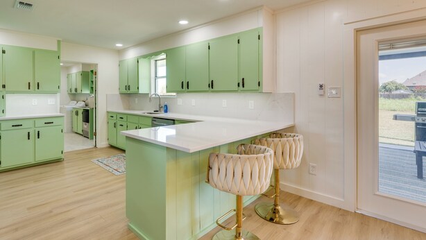 A modern kitchen with green cabinets, a white countertop, and a bar area with cushioned stools. - Furnished Patio & Spacious Yard! Seguin Escape (Seguin)