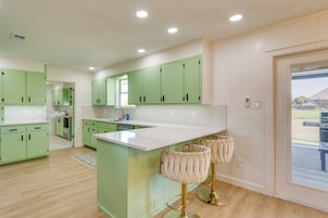 A modern kitchen with green cabinets, a white countertop, and a bar area with cushioned stools.