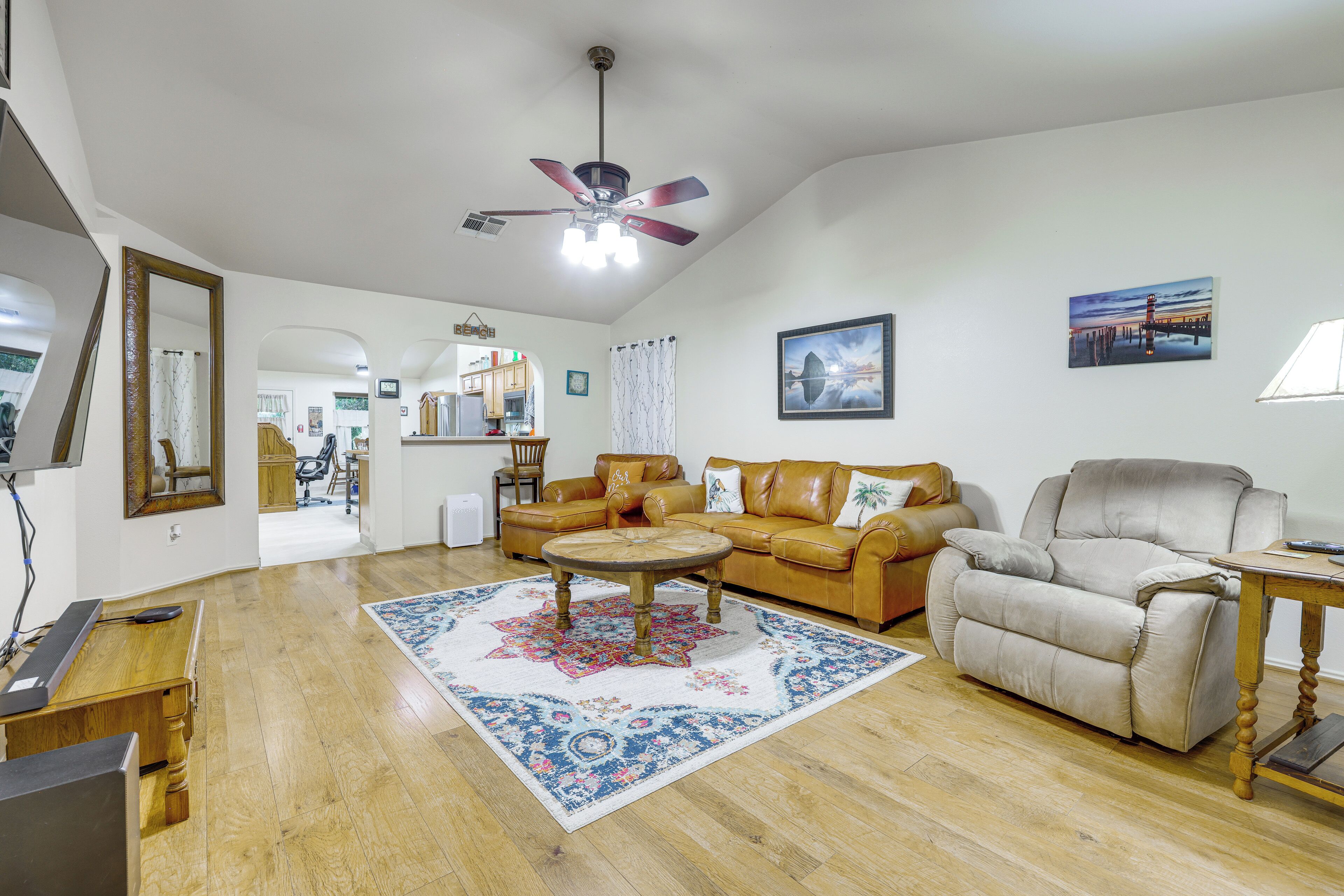 Un salon spacieux avec un ventilateur de plafond, un canapé en cuir marron, un fauteuil beige et une table basse.
