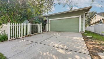 A residential garage with a green door, a white picket fence, and a tree in the background.