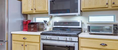 A kitchen with wooden cabinets, a stainless steel refrigerator, a microwave, a stove, and a toaster.
