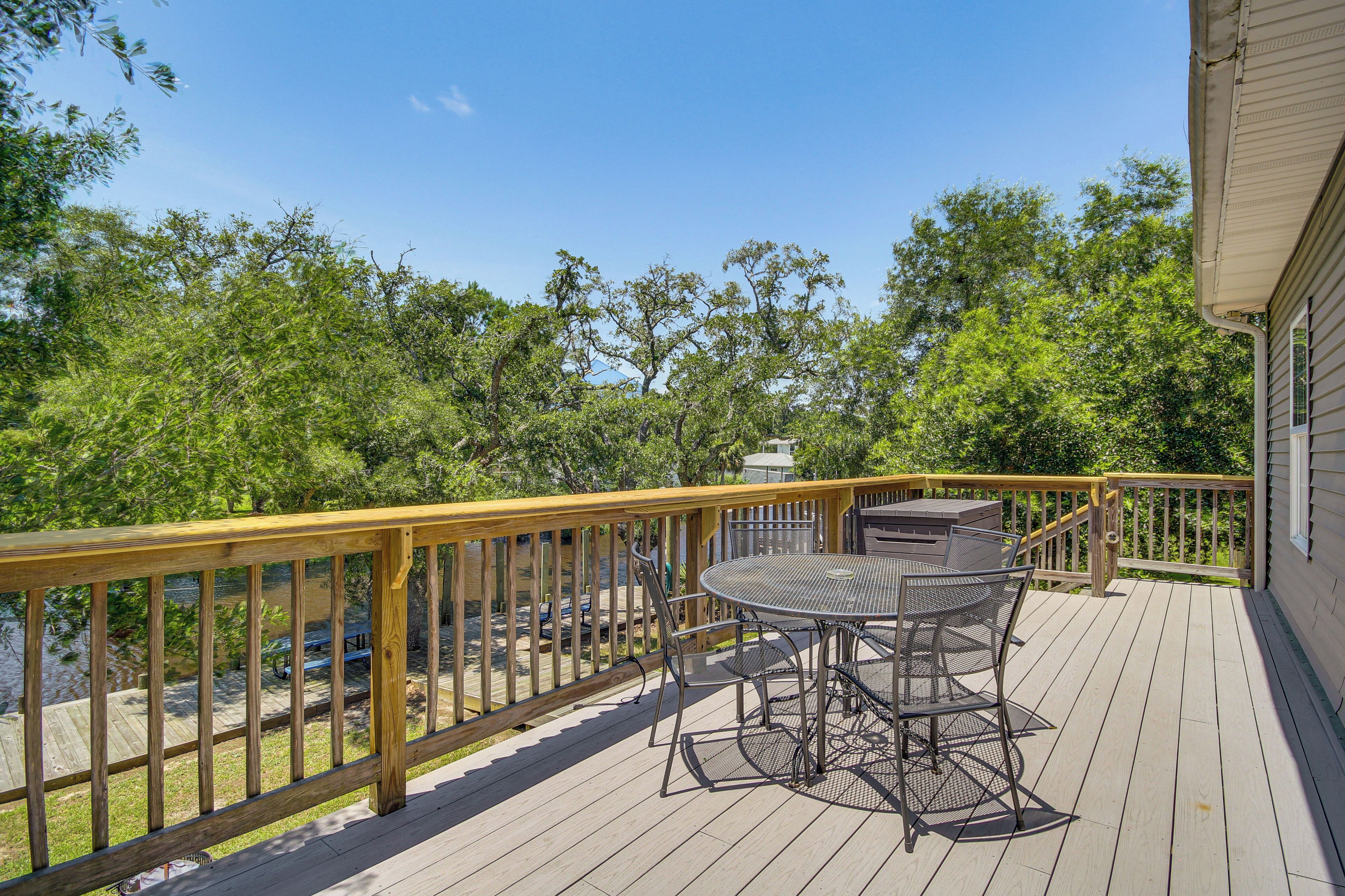 A wooden deck with a table and chairs, overlooking a body of water and surrounded by trees.