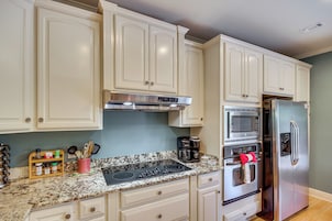 Una cocina con armarios blancos, un refrigerador de acero inoxidable, un microondas y una cafetera.