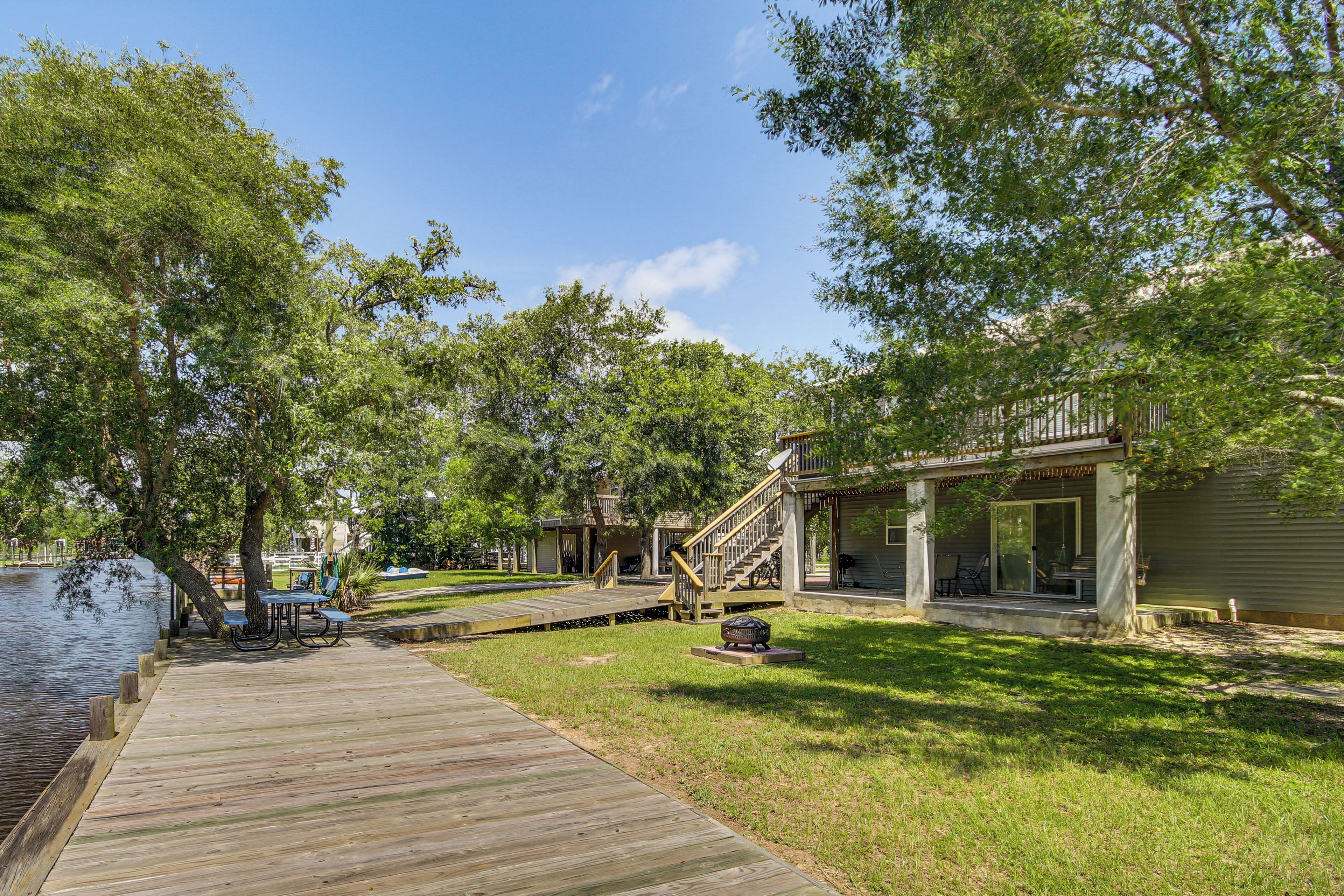 A wooden dock leading to a grassy area with picnic tables and a barbecue grill.