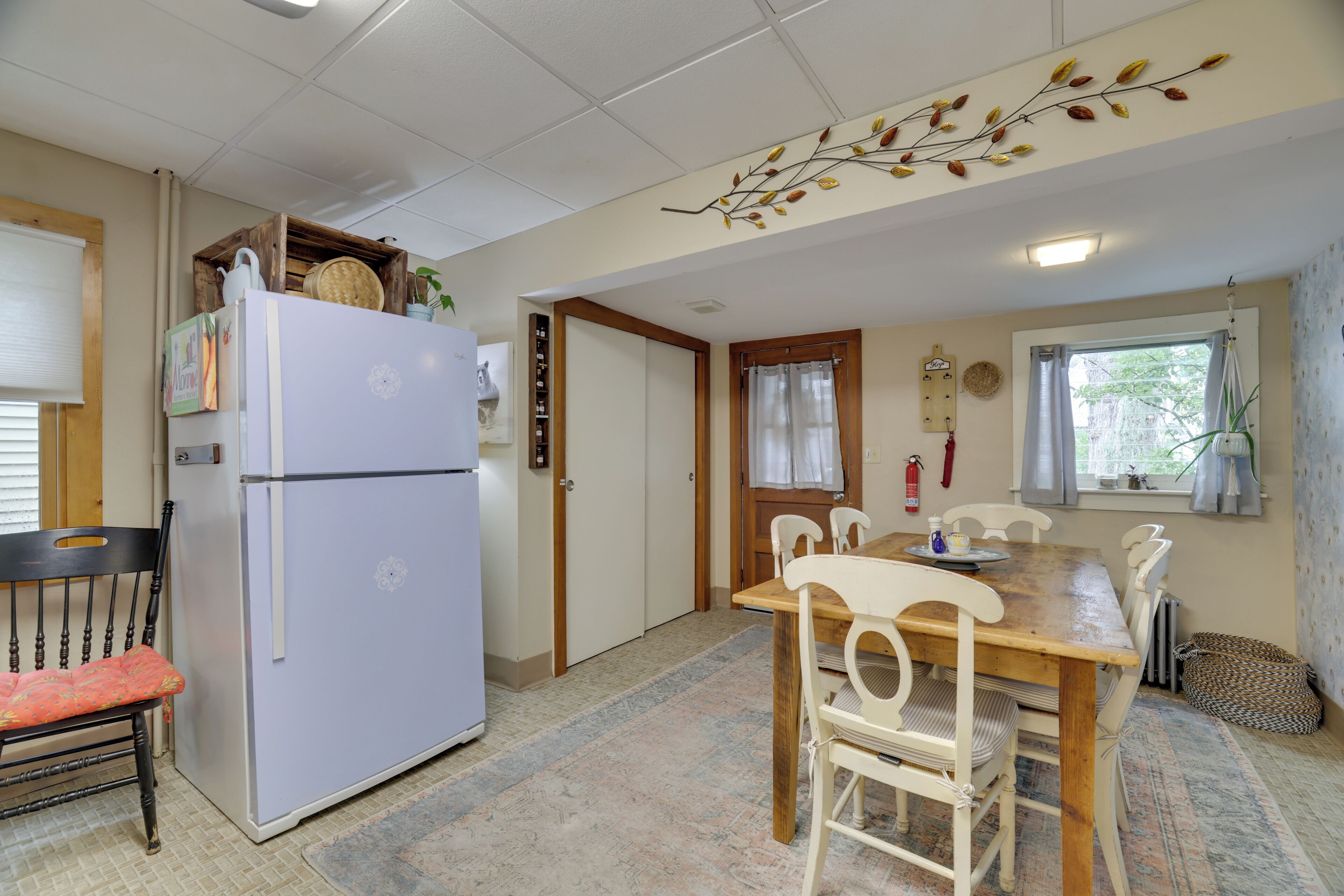 Cocina compacta con refrigerador, una mesa de comedor con sillas y una ventana con cortinas.