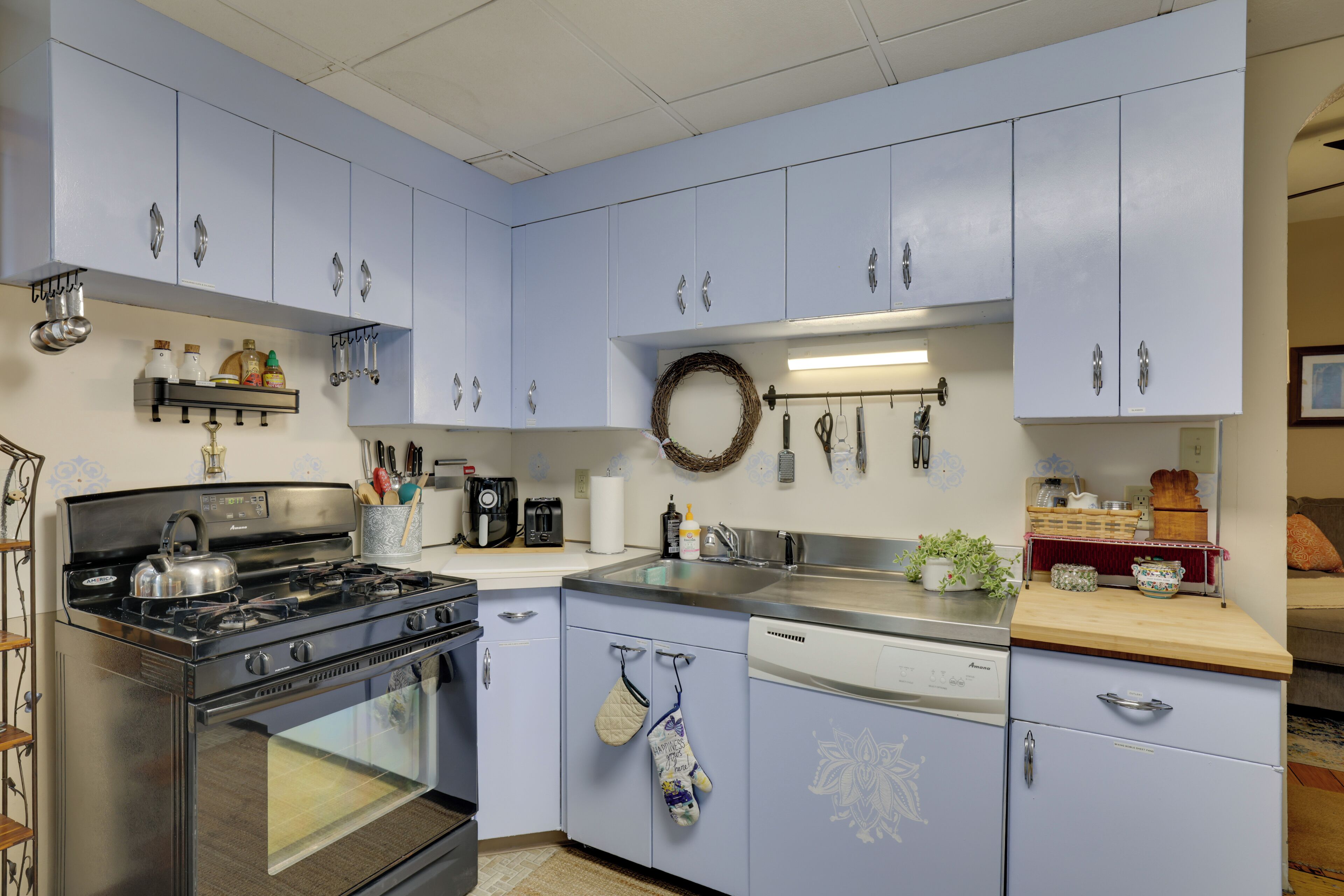 Una cocina con gabinetes azul claro, una estufa, un lavavajillas y diversos utensilios de cocina.