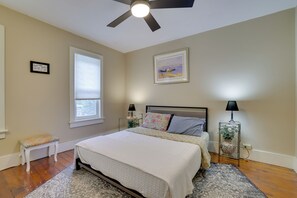 A bedroom with a bed, bedside tables, a ceiling fan, a window, and a painting on the wall. - Walk to Main St Stroudsburg! Historic Dtwn Home (Stroudsburg)