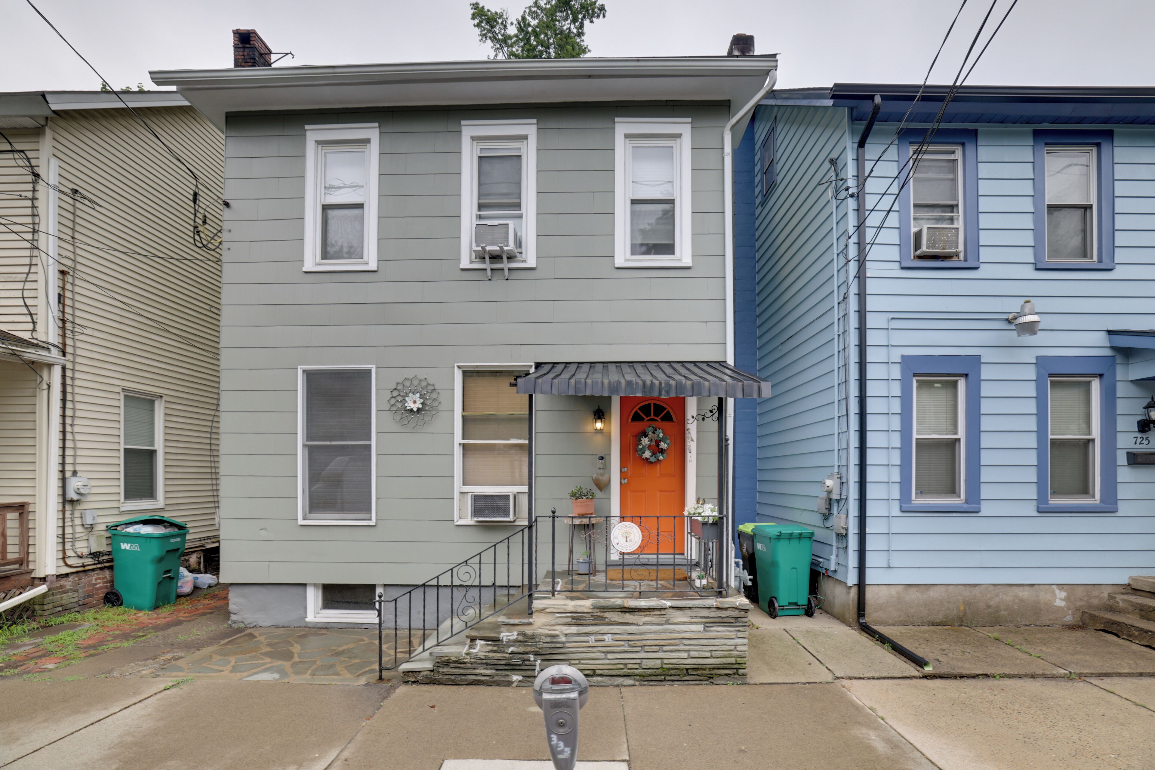 A two-story residential building with a front porch, a mailbox, and a parking meter.