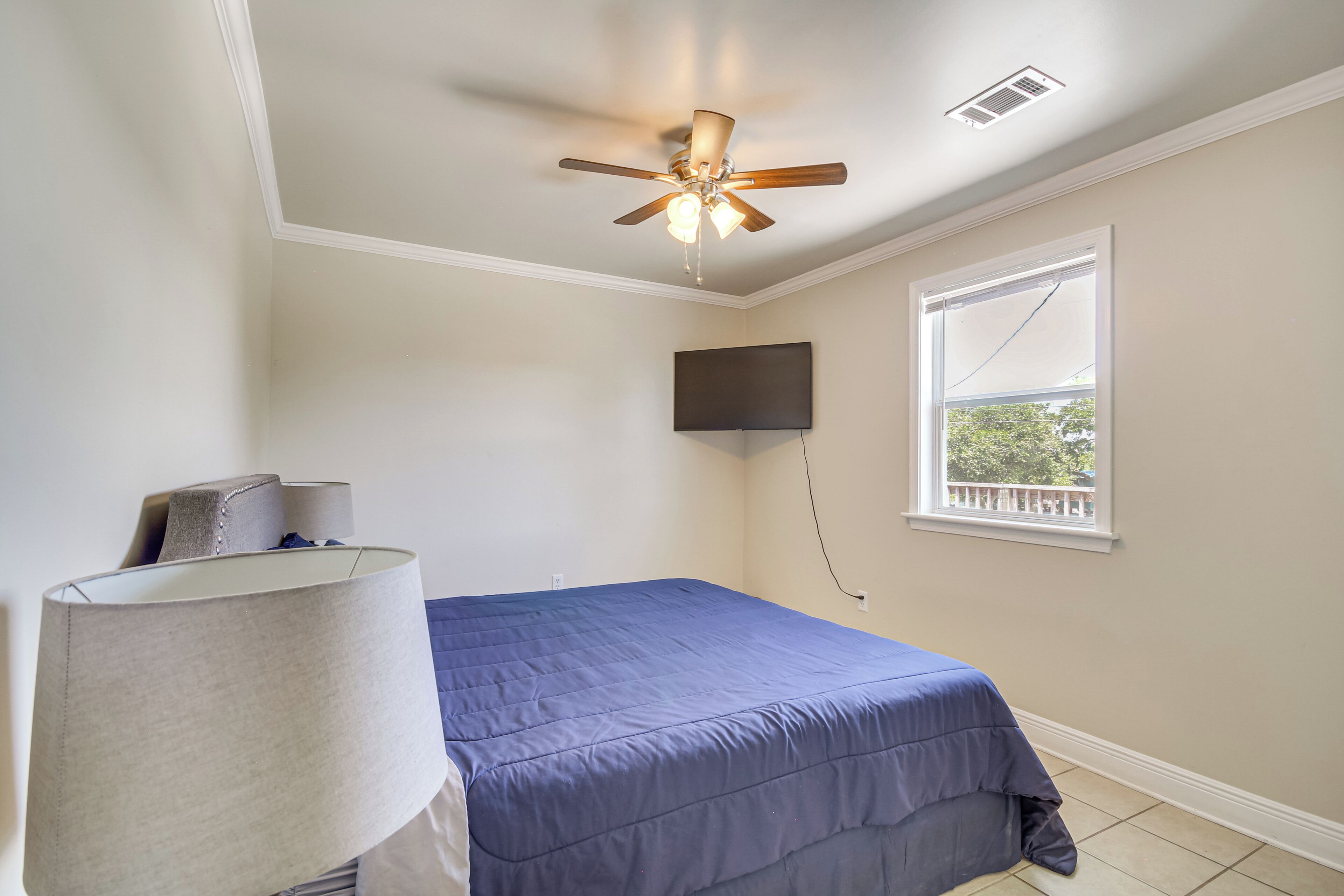 Un dormitorio con cama, ventilador de techo, televisor montado y ventana con vista.