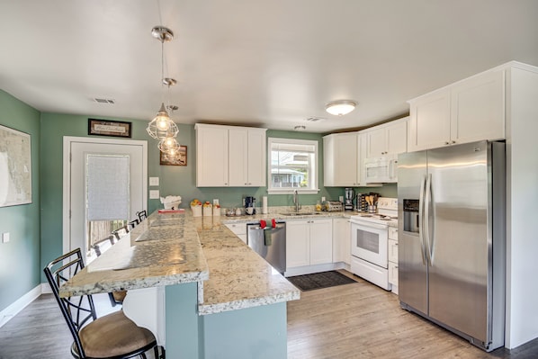 A modern kitchen with white cabinets, a stainless steel refrigerator, and a marble countertop. - Canal & Boat Launch: Bay St Louis Group Getaway (Bay St Louis)