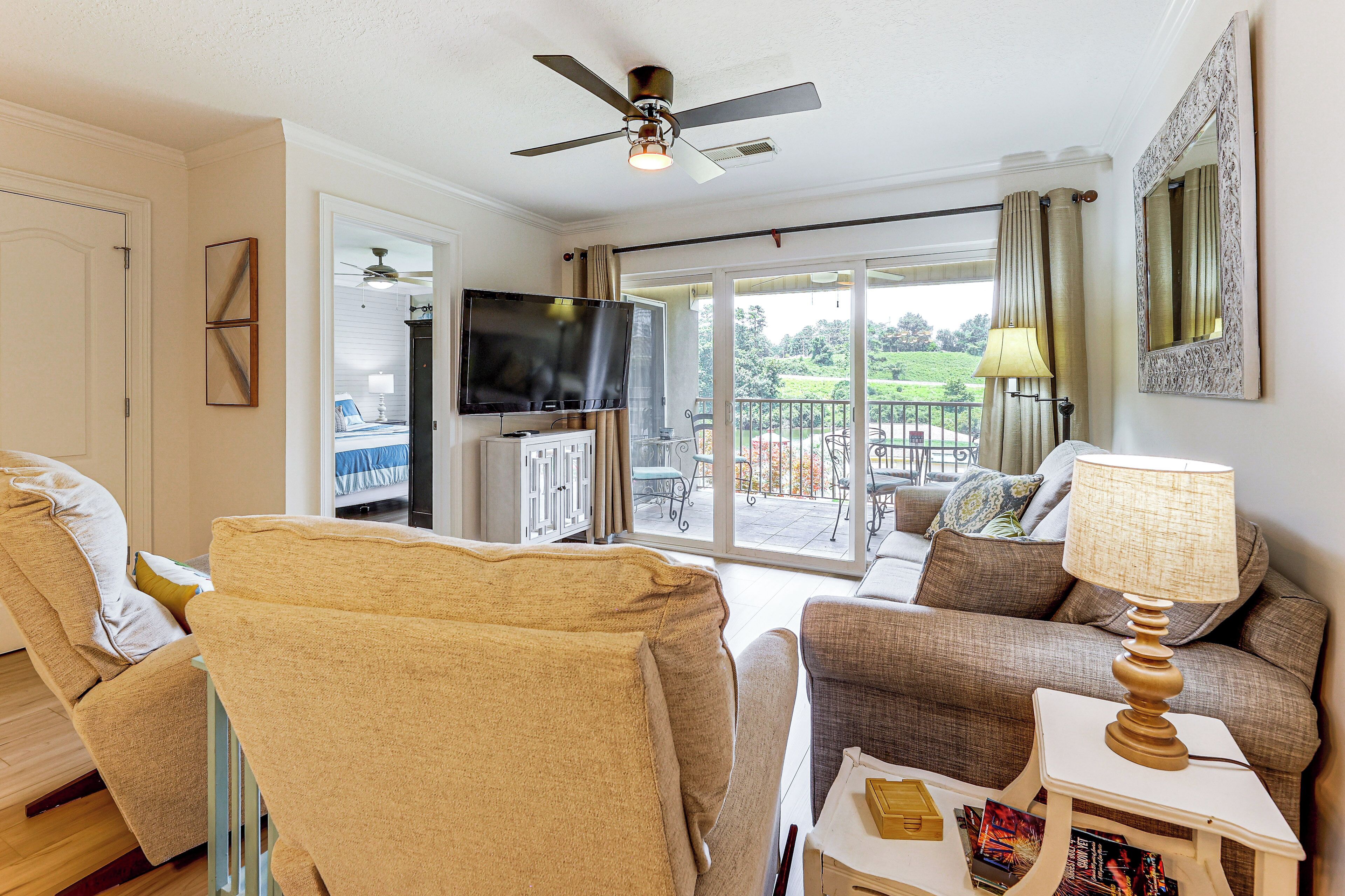 A living room with a ceiling fan, a flat-screen TV, a sofa, a chair, and a table with a lamp.