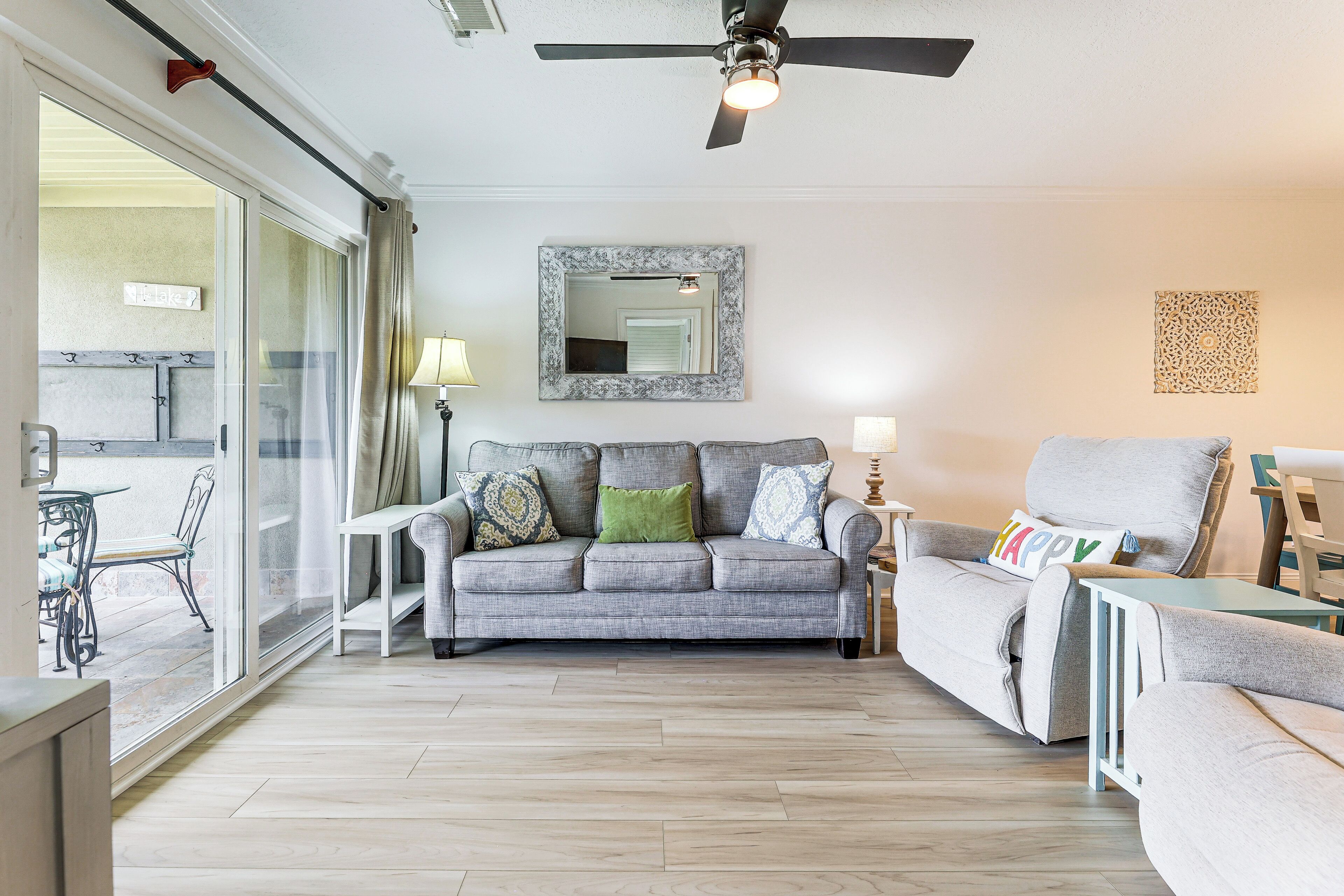 A living room with a grey sofa, a green pillow, a white lamp, and a ceiling fan.
