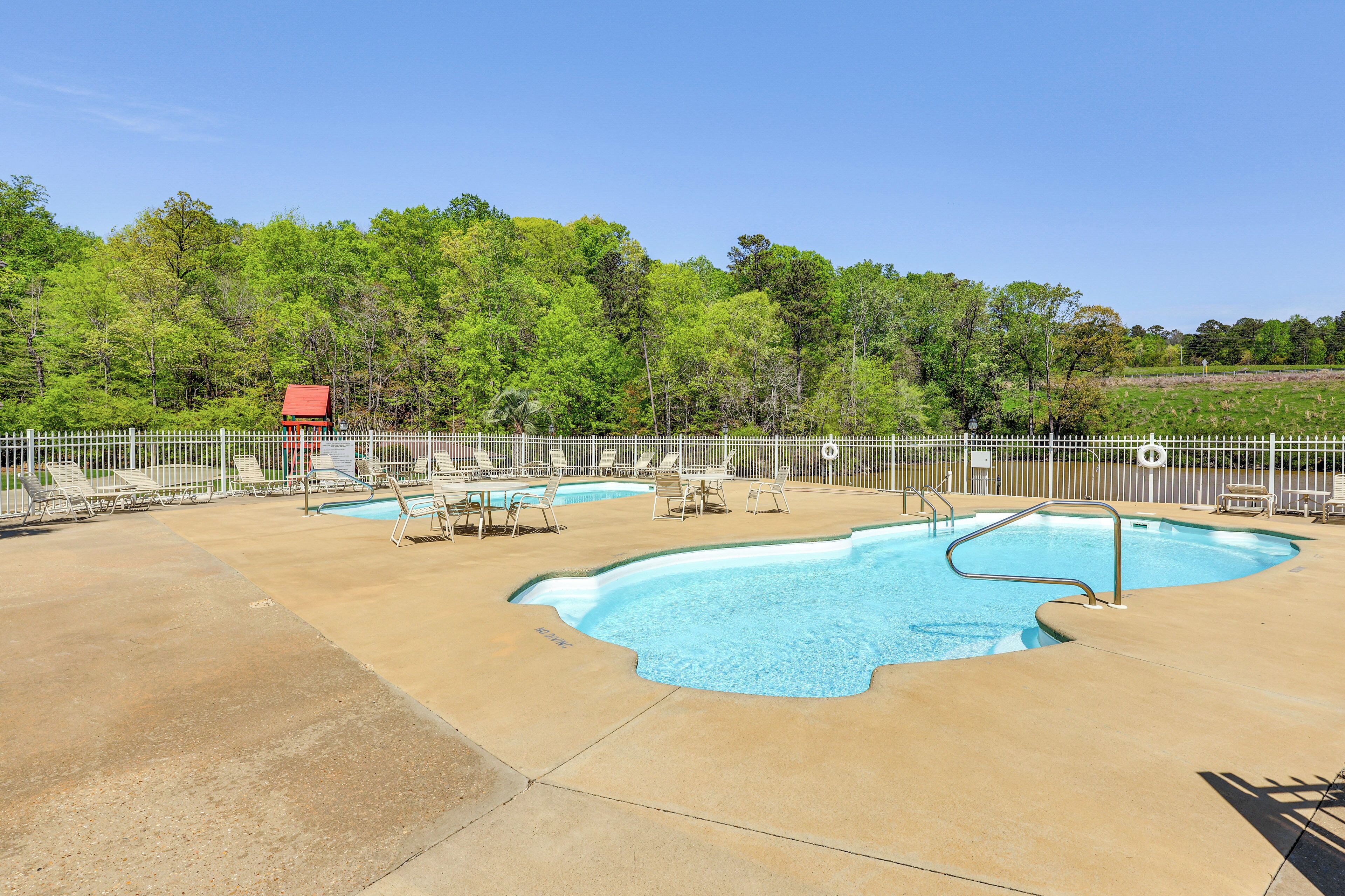 A swimming pool with a white fence, lounge chairs, and a red building in the background.