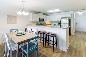 A modern kitchen with white cabinetry, a central island, bar stools, and a dining table with chairs.
