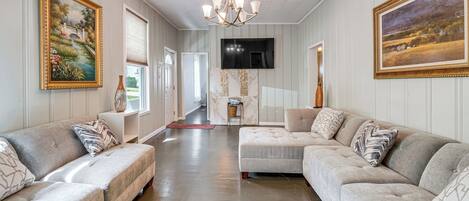 A spacious living room with a large sectional sofa, a chandelier, and artwork on the walls.