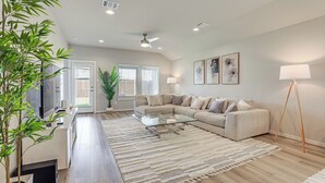 Ein stilvolles Wohnzimmer mit einer Eckcouch, einem Glastisch, einem großen Teppich und einer Zimmerpflanze.