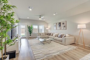 Uma sala de estar moderna com um sofá de canto, uma mesa de centro de vidro, um tapete grande e um vaso com planta.