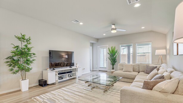 Ein modernes Wohnzimmer mit einem Flachbildfernseher, einem Glastisch, einem beige farbenen Sofa und einem großen Teppich.