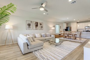 Uma sala de estar moderna com um sofá, mesa de centro e luminárias de chão. Há uma área de refeições com uma mesa e cadeiras.