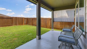 A covered patio area with a wooden fence, a concrete floor, and wicker furniture.