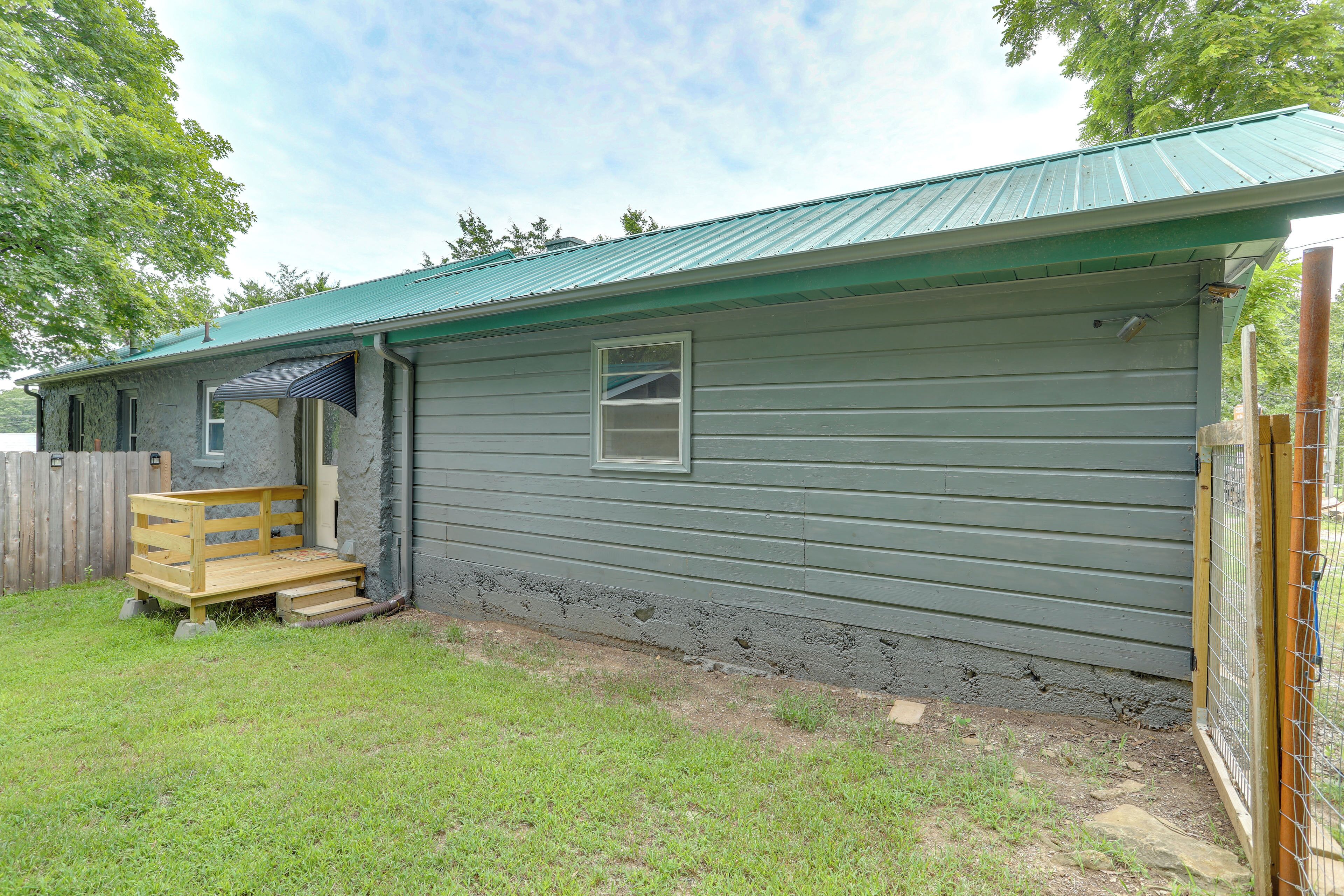 A single-story house with a green metal roof, a front porch with a bench, and a small window.