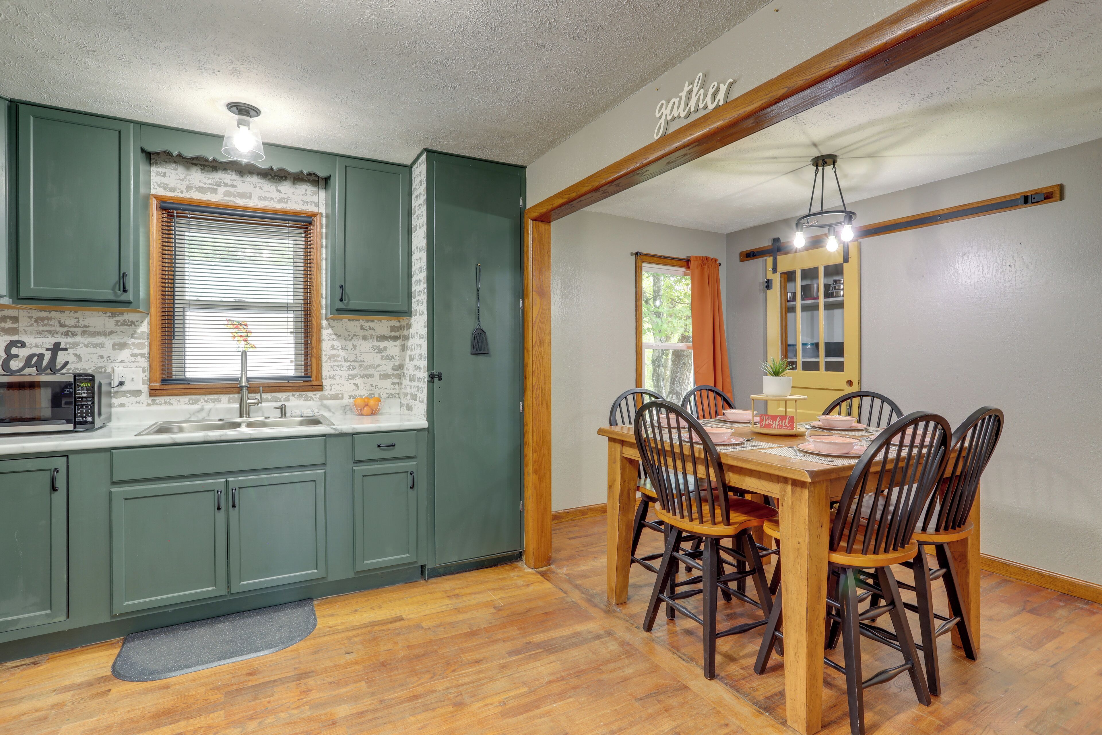 A kitchen with green cabinets, a microwave, and a dining area with a wooden table and chairs.