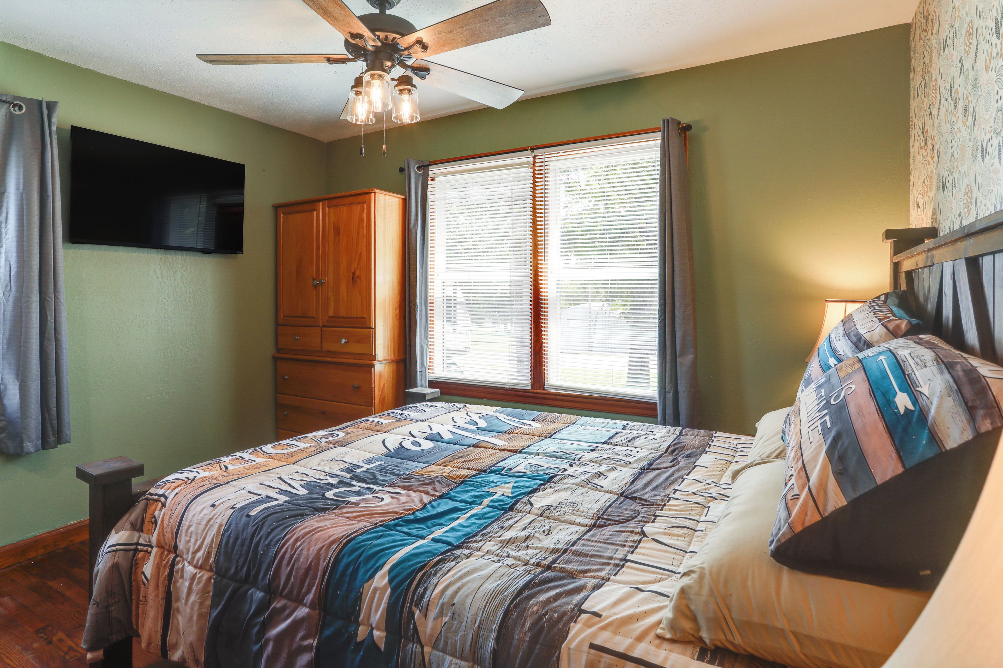 A bedroom with a bed, a wooden wardrobe, a ceiling fan, and a window with blinds.
