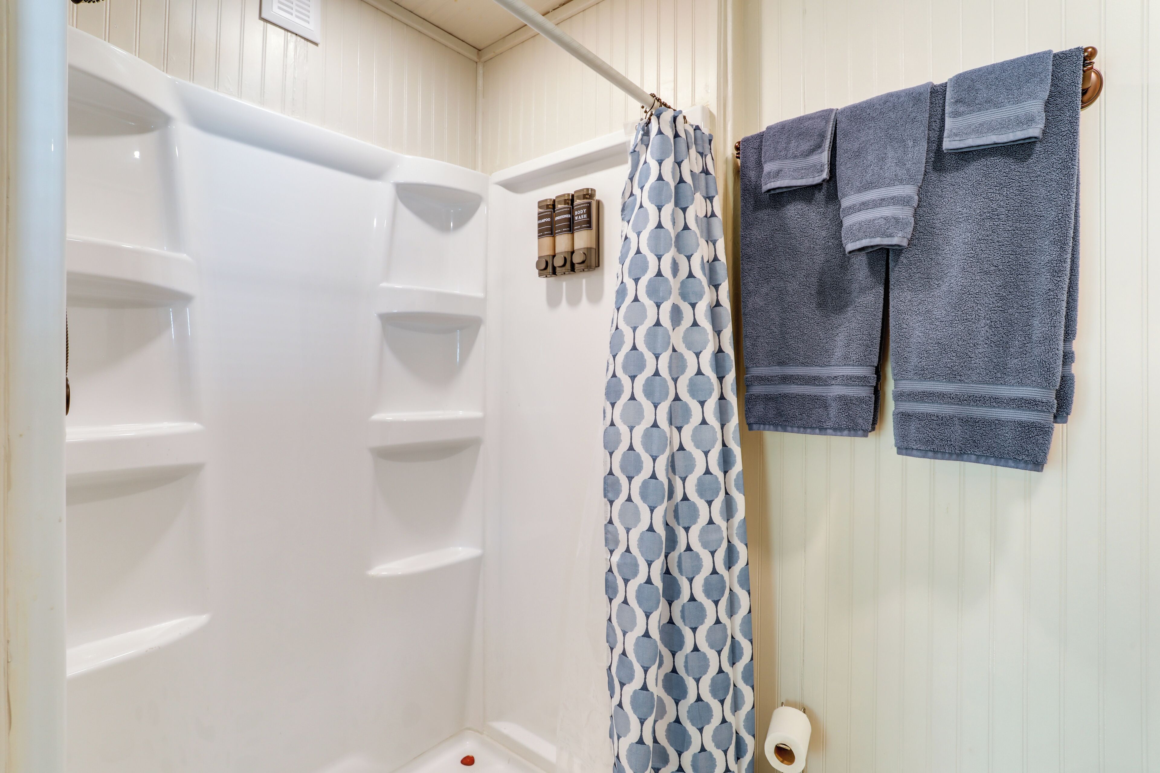 A shower with a white tub and a patterned shower curtain. There are two towels hanging on a towel rack.