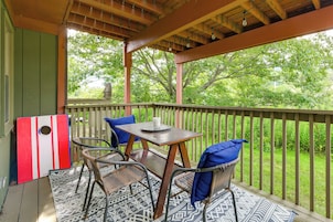 Un espacio de estar al aire libre techado con una mesa, sillas, un adorno de pared y vista a follaje.