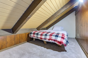 Una habitación pequeña e inclinada con una cama individual, cabecera de madera y techo color beige.