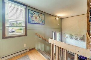 Una escalera con barandilla de madera, una ventana con persianas y una pared con dos cuadros.